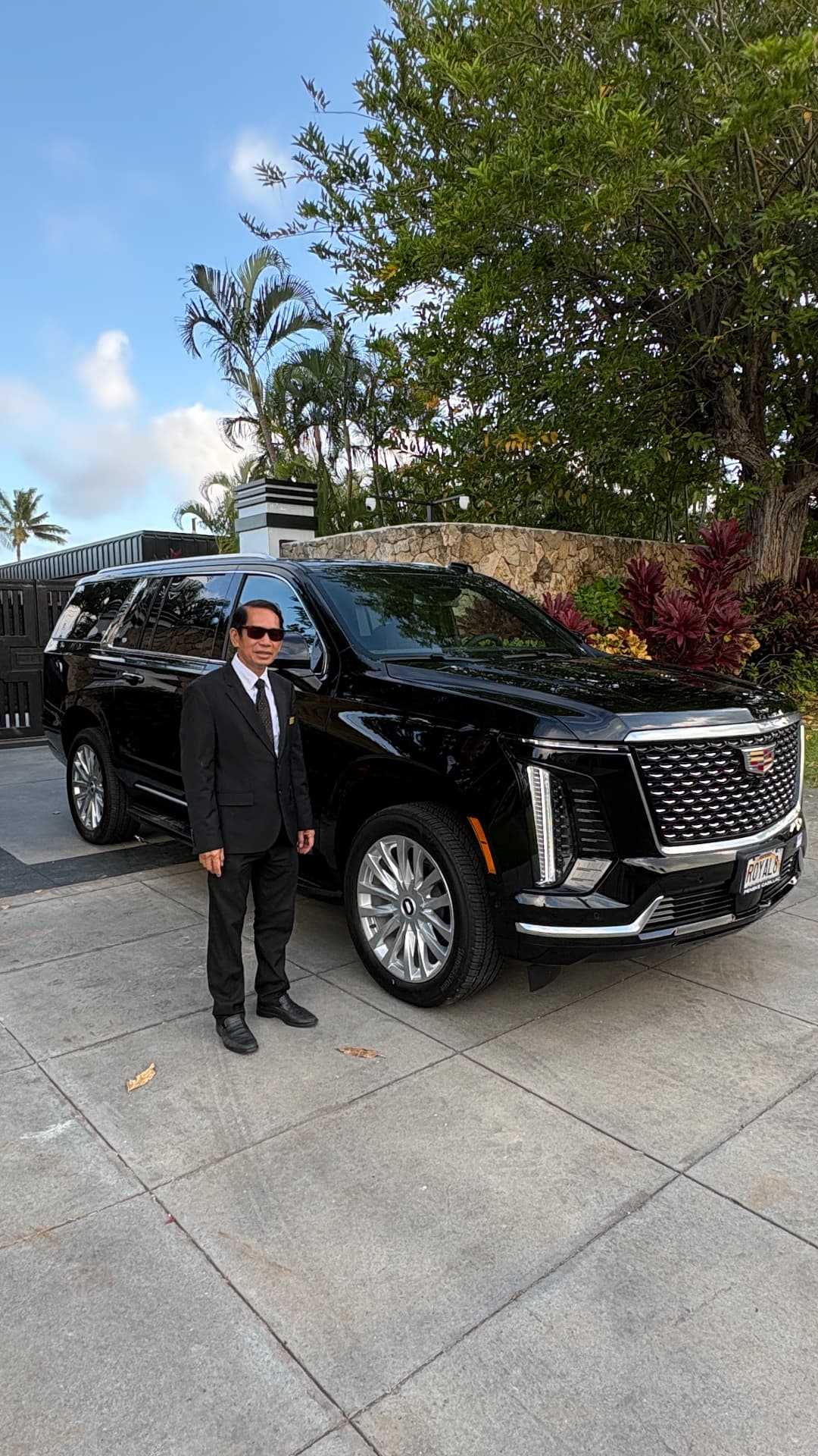 AURA chauffeur standing beside a black Cadillac Escalade at a Hawaii estate gate