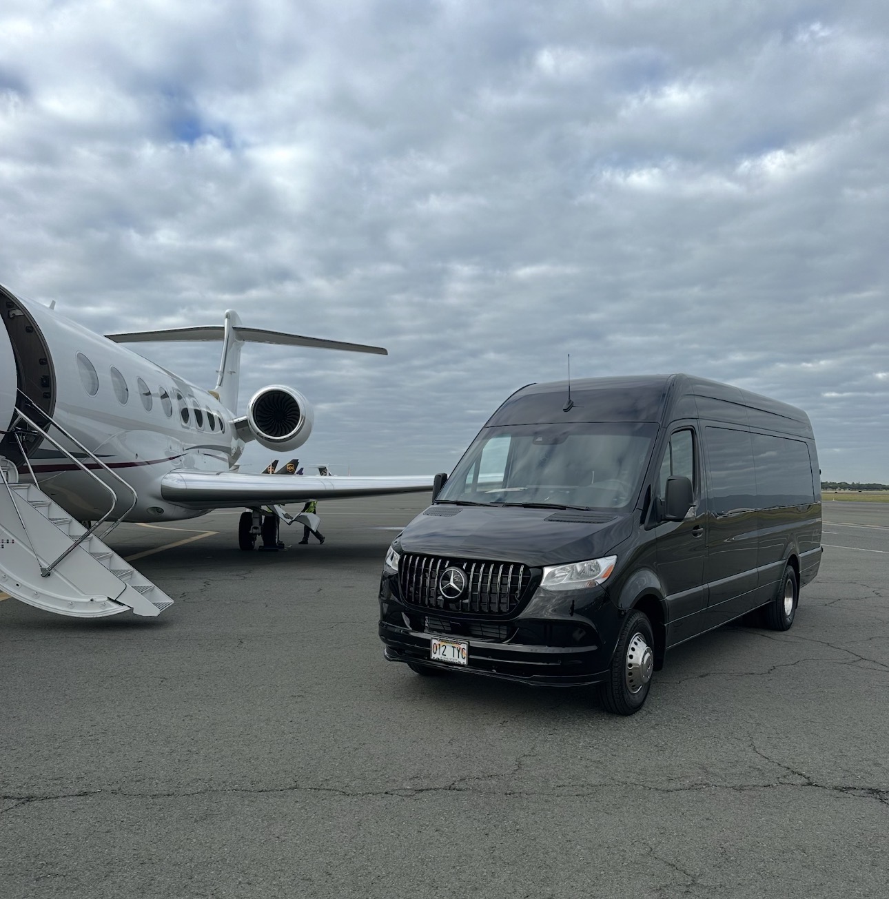Black Mercedes Sprinter parked beside a private jet on the tarmac
