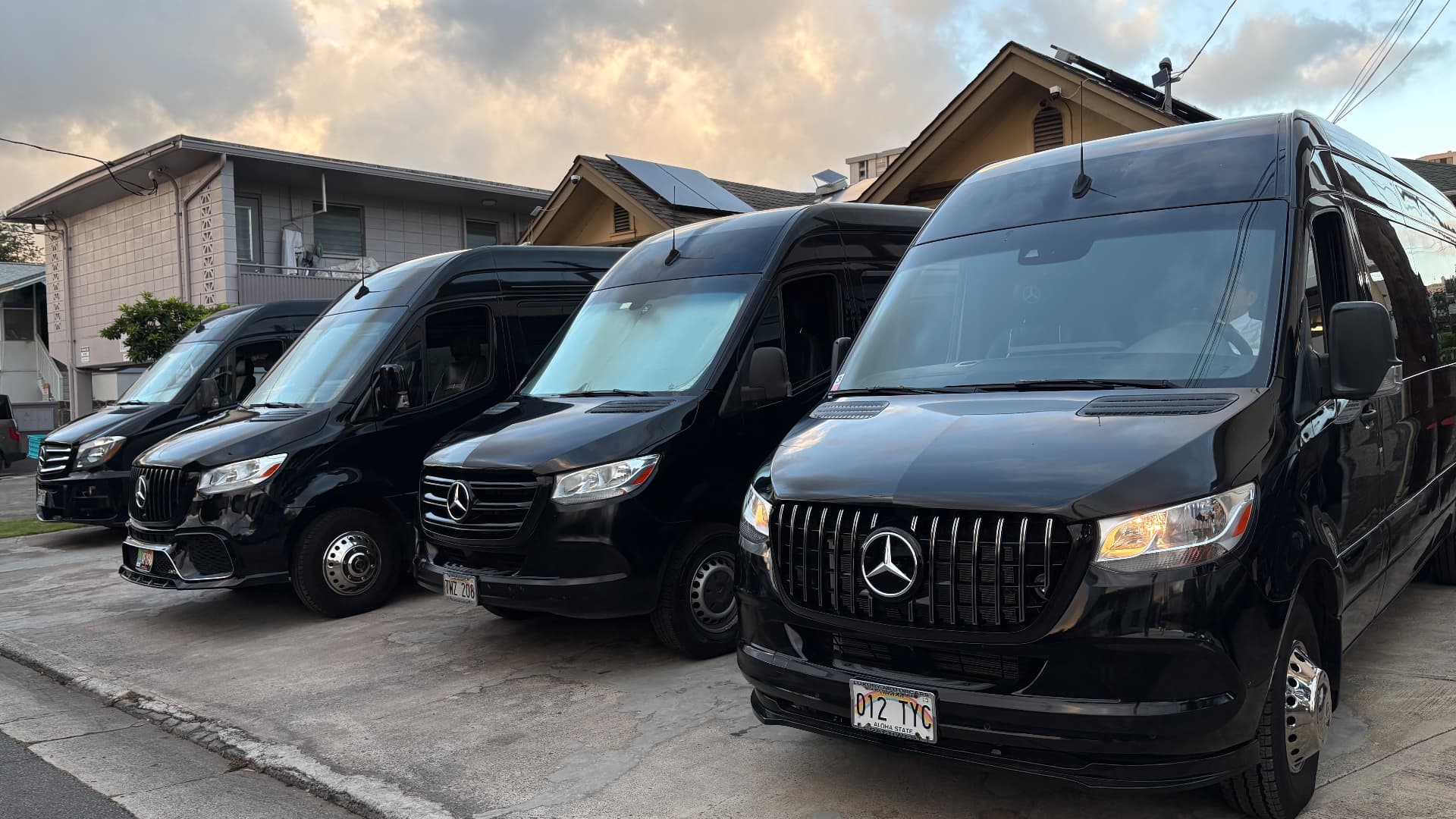 Four black Mercedes Sprinter vans lined up at sunrise in Honolulu